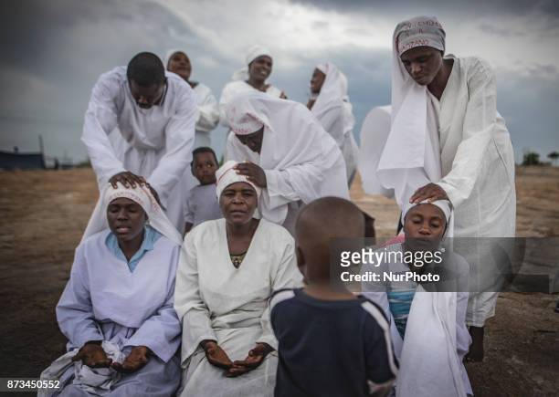 Apostolic church members recieve blessings while a child watches. Apostolic Christians conduct a religious service in a piece of open land in the...