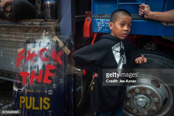 Child stands next to a riot police shield with a graffiti after protesters clash with riot police as they march the streets of Manila during the...