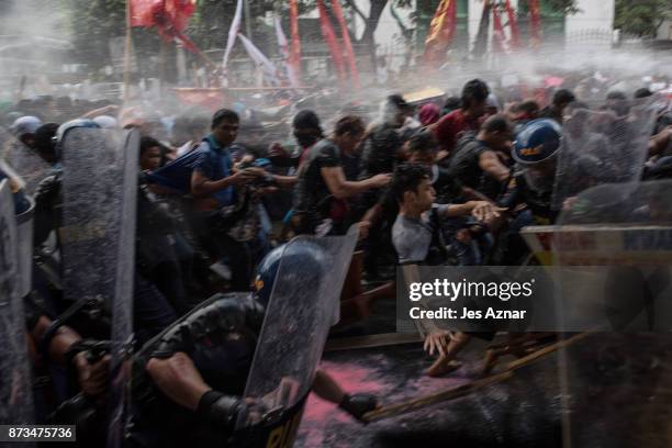 Protesters are soaked as they clash with riot police as they march the streets of Manila during the start of the ASEAN meetings between heads of...