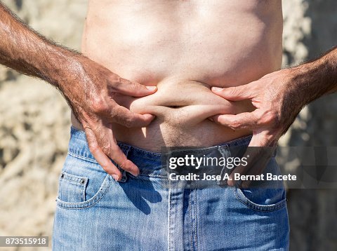 A close-up image of a men mature with belly fat pinching itself, white-skinned, with jeans shorts in the light of the Sun in the beach A close-up image of a men mature with belly fat pinching itself, white-skinned, with jeans shorts in the light of the Sun in the beach