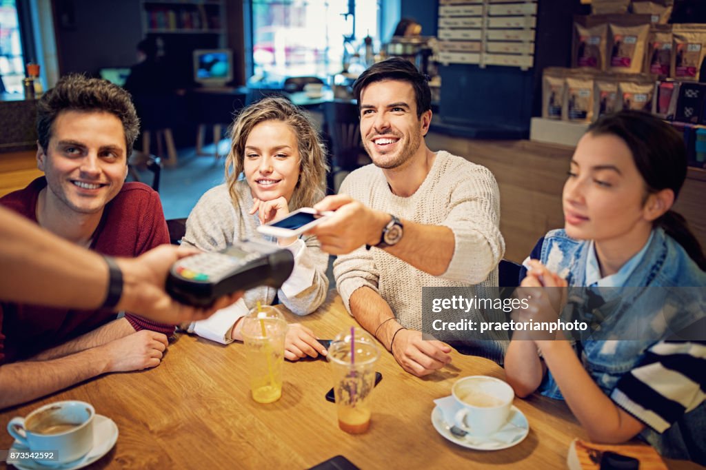 Groupe d’amis paient à l’aide de téléphone portable dans le café