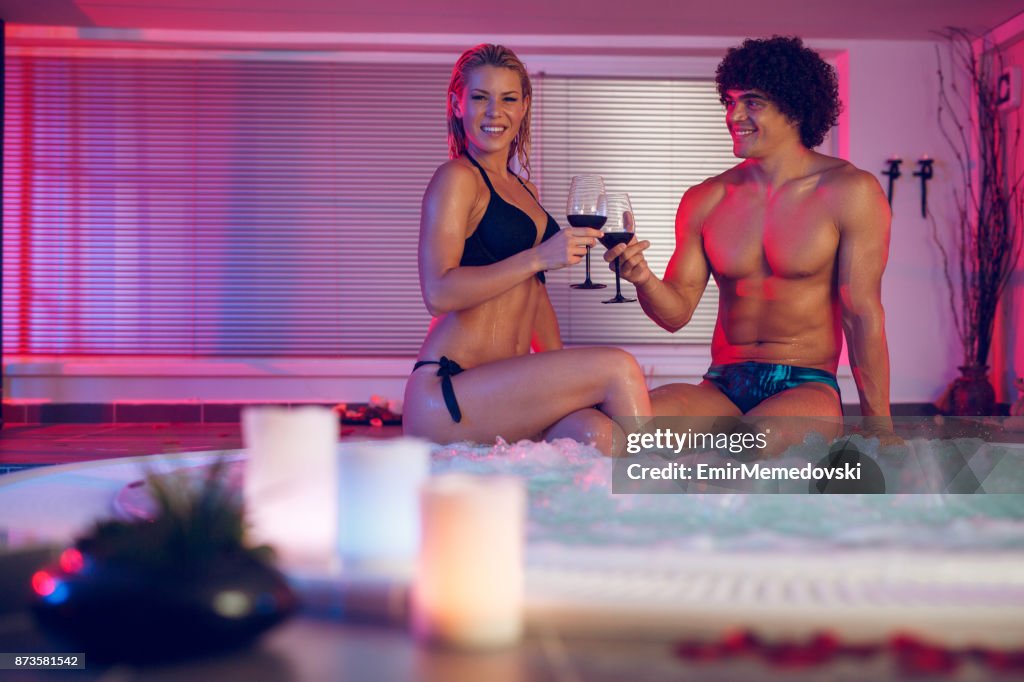 Cheerful couple toasting with red wine in a hot tub.