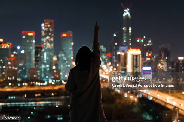 young female standing in front of modern city - angeleuchtet zahlen mensch stock-fotos und bilder