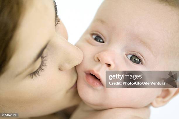 mother kissing infant on the cheek, baby looking at camera - extreme close up kiss stock pictures, royalty-free photos & images