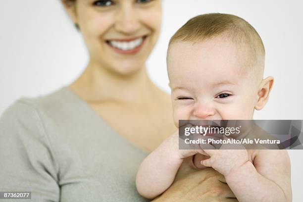 mother holding infant, baby sticking hand in mouth, looking at camera - bébé grimace photos et images de collection