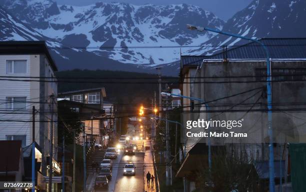 People walk down a street at dusk on November 7, 2017 near Ushuaia, Argentina. Ushuaia is situated along the southern edge of Tierra del Fuego, in...