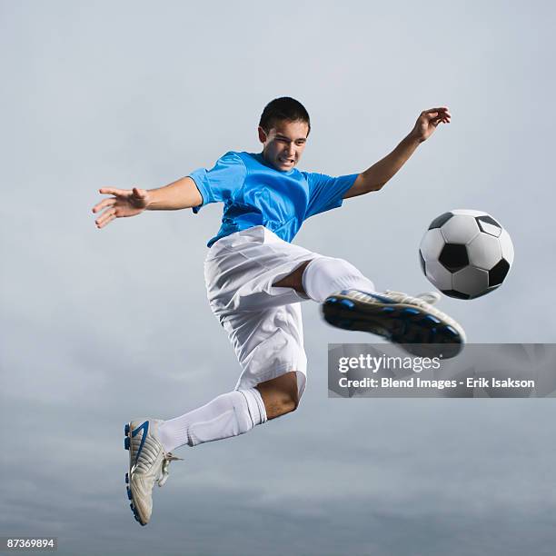 mixed race teenager in mid-air kicking soccer ball - teenage soccer player stock pictures, royalty-free photos & images