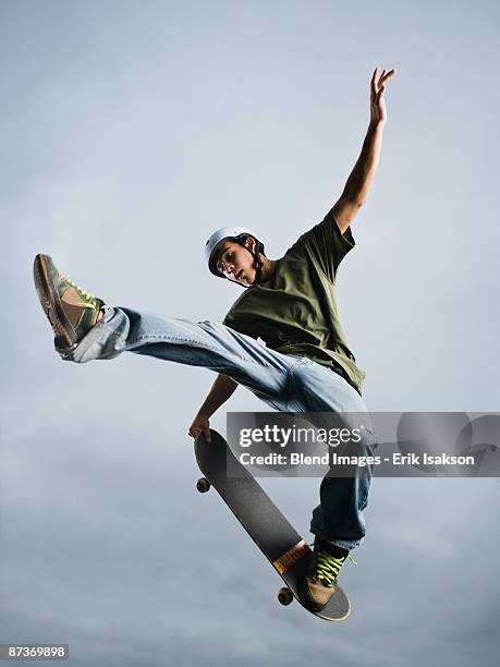 mixed race teenager in mid-air on skateboard - skate stock-fotos und bilder