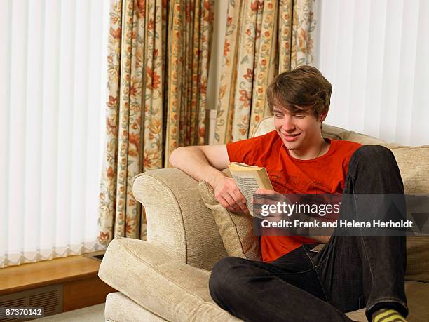 young man relaxing on sofa reading book - croyde imagens e fotografias de stock