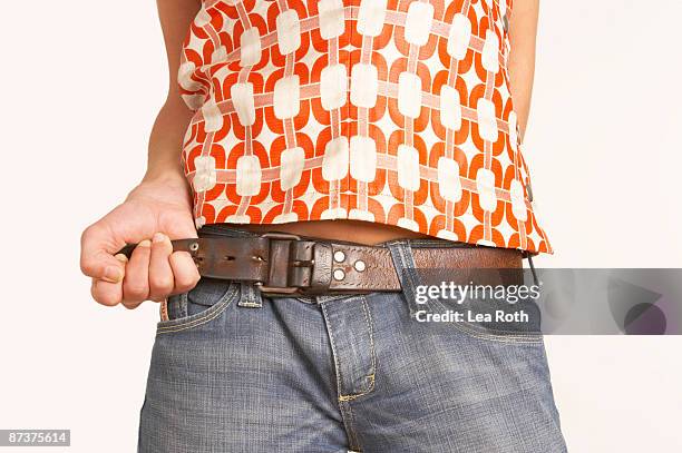 close-up of young woman pulling belt of her jeans - cintura foto e immagini stock