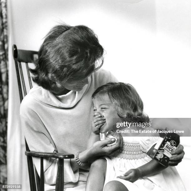 View of Jacqueline Kennedy as she holds her daughter Caroline as the latter eats cereal, Hyannis Port, Massachusetts, Spring or Summer 1959. The...