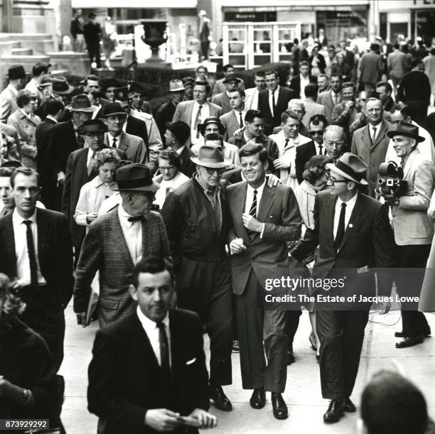Surrounded by journalists, staffers, and members of the public, Senator John F Kennedy smiles as he walks with an unidentified man during a campaign...