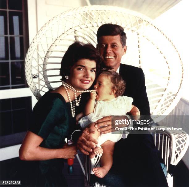 Portrait of married couple Jacqueline Kennedy and Senator John F Kennedy as they pose with their daughter Caroline, who attempts to eat her mother's...