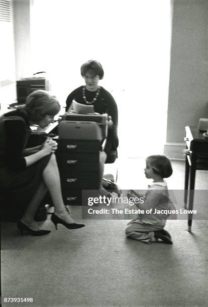 Pair of unidentified White House secretaries talk with the President's daughter Caroline Kennedy who kneels on the floor, Washington DC, March 1961.