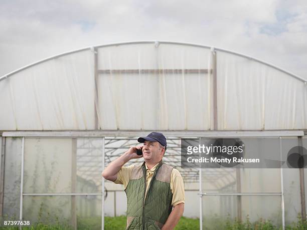 farmer on mobile outside polytunnel - answering stockfoto's en -beelden