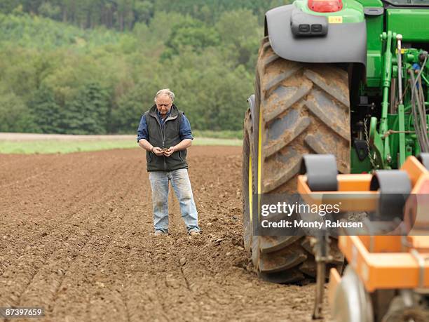 farmer examining soil in field - tractor ploughing field bildbanksfoton och bilder