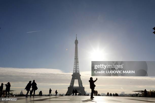 Tourists pose for photographs at the Parvis des droits de l'homme in front of the Eiffel Tower in Paris on November 14, 2017.