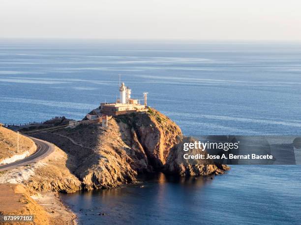 sunset on the beach and rocky coast with the silhouette of big cliffs and a 	lighthouse . cabo de gata - nijar natural park, sirens reef, biosphere reserve, almeria,  andalusia, spain - lighthouse reef - fotografias e filmes do acervo