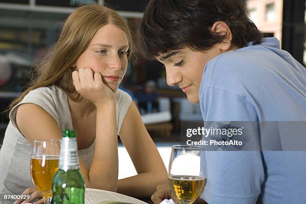 young couple sitting at outdoor cafe, looking down at book - peinlich stock-fotos und bilder