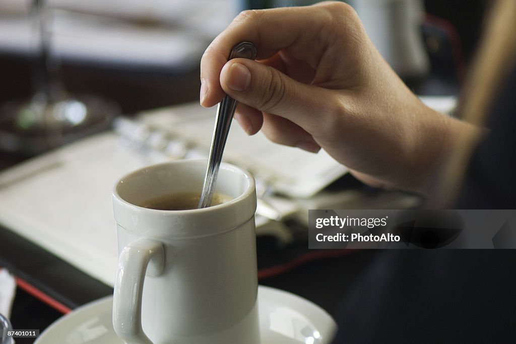 Hand stirring coffee, agenda on table in background, close-up