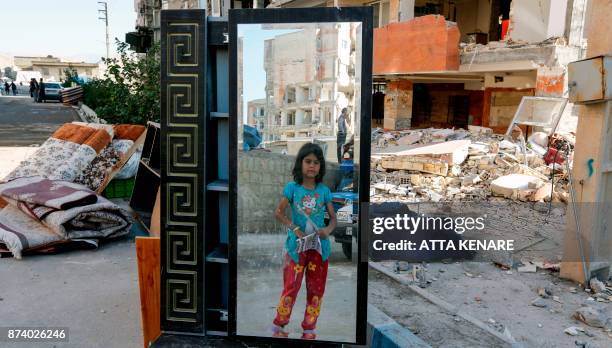 An Iranian girl looks through a salvaged mirror from a damaged building in the town of Sarpol-e Zahab in the western Kermanshah province near the...
