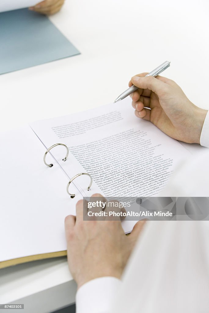 Man reviewing document in binder, over the shoulder view, cropped