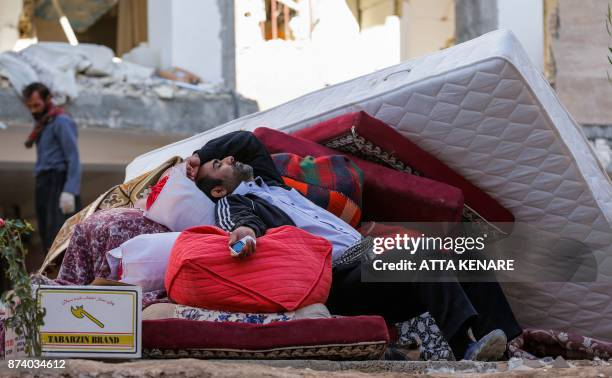 An Iranian man rests as he lies atop salvaged mattresses and items outside damaged buildings in the town of Sarpol-e Zahab in the western Kermanshah...