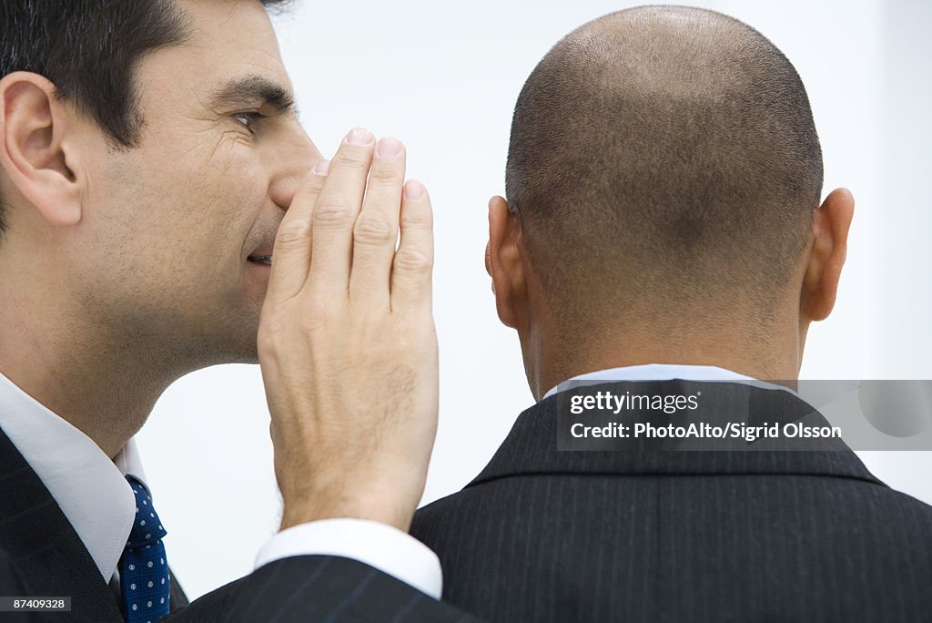 Businessman whispering in colleague's ear, close-up