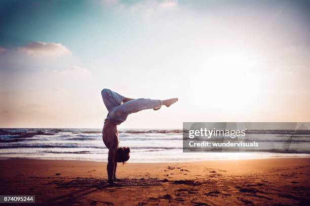 sportlicher mann üben yoga am strand bei sonnenuntergang - beach yoga stock-fotos und bilder