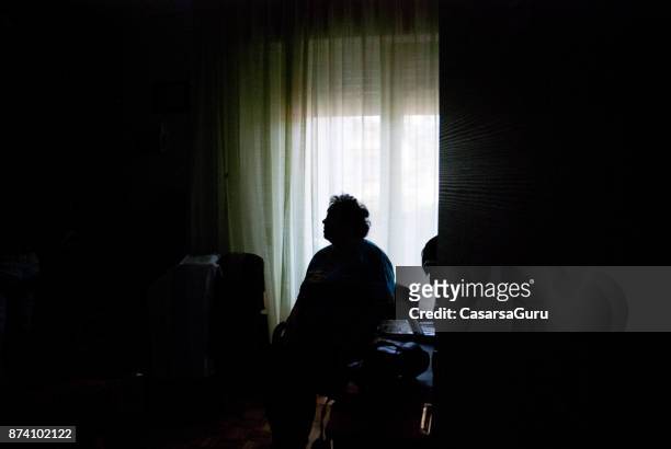 senior woman alone in dark room - loneliness stock pictures, royalty-free photos & images