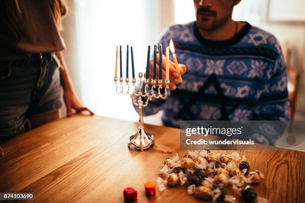 young man lighting candlesticks on traditional jewish menorah for hanukkah - menorah imagens e fotografias de stock