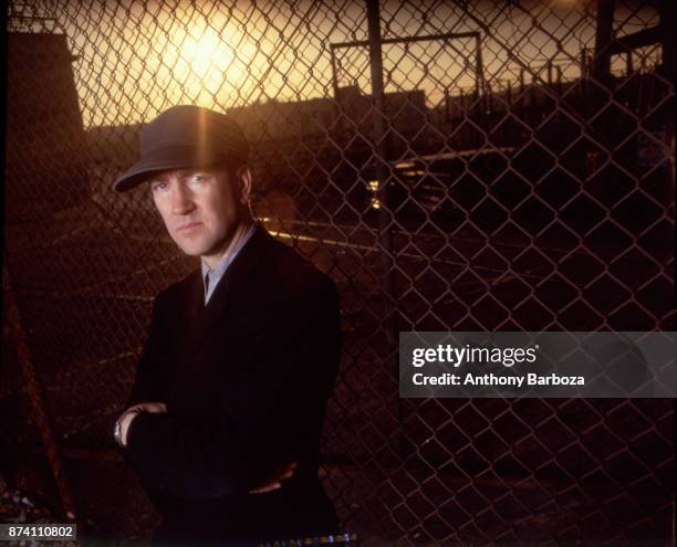 Portrait of American film and television director David Lynch, his arms folded, as he poses in front of a chain-link fence, Los Angeles, California,...