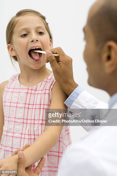 doctor examining a girl's throat using a tongue depressor - girl tongue doctor stockfoto's en -beelden