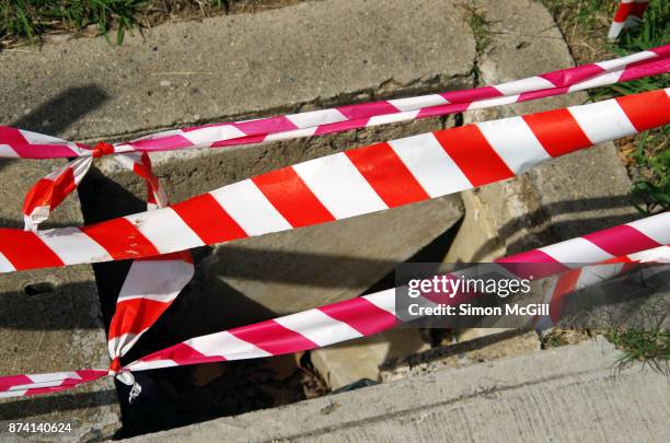 red and white striped plastic cordon tape around a utility access point with a broken cement cover - makeshift fix stock pictures, royalty-free photos & images