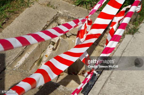 red and white striped plastic cordon tape around a utility access point with a broken cement cover - makeshift fix stock pictures, royalty-free photos & images