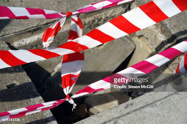 red and white striped plastic cordon tape around a utility access point with a broken cement cover - behelfsmäßig stock-fotos und bilder
