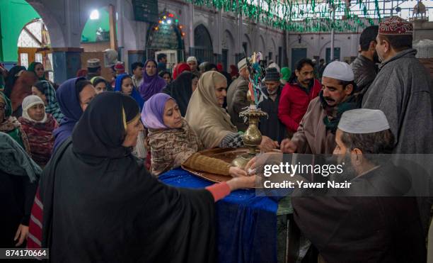 Kashmiri Muslim man distributes sweets to the women devotees pray at the shrine of the Sufi saint Sheikh Hamza Makhdoom during a festival on November...