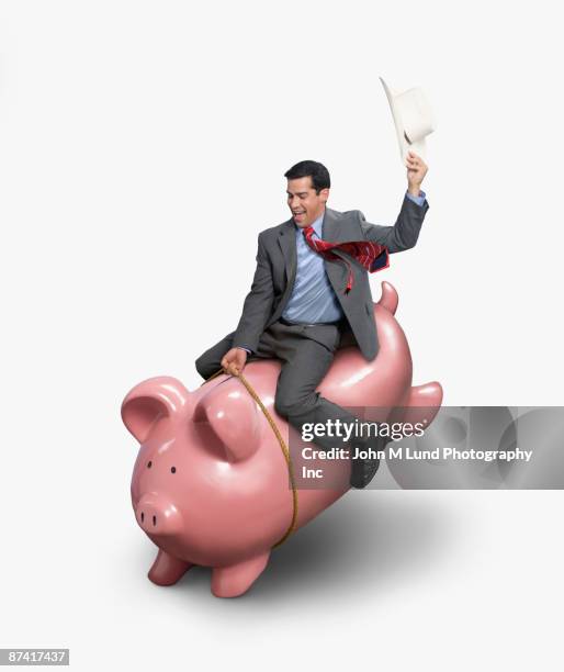 hispanic businessman riding piggybank - cavalo selvagem arqueado imagens e fotografias de stock
