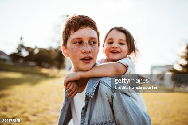 two lovely kids piggyback at the park - sibling stock pictures, royalty-free photos & images