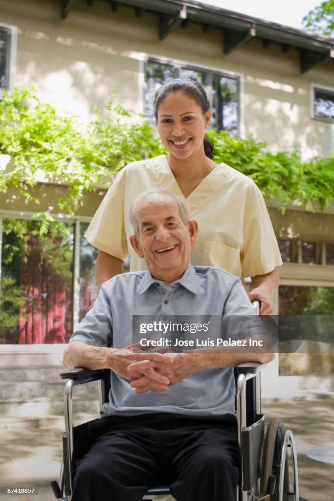 Senior Hispanic man outdoors in wheelchair with aide