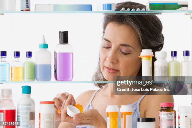 hispanic woman taking medication in bathroom - bathroom cabinet stock pictures, royalty-free photos & images