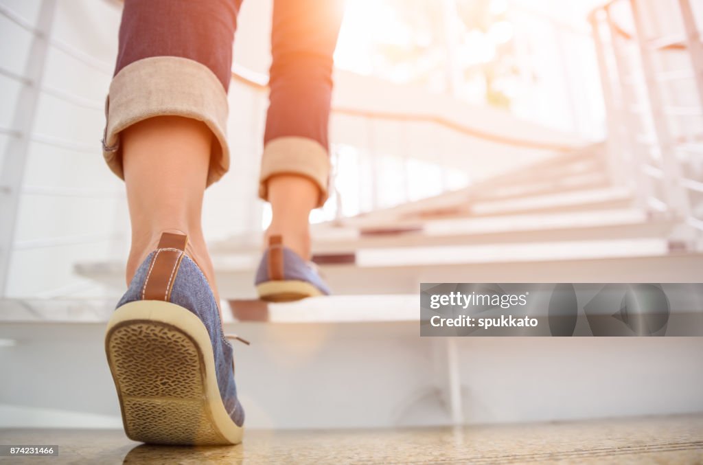 Young adult woman walking up the stairs with sun sport background.