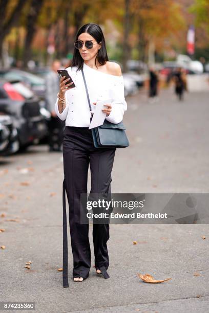 Guest wears sunglasses, an off shoulder white top, black pants, outside Lanvin, during Paris Fashion Week Womenswear Spring/Summer 2018, on September...