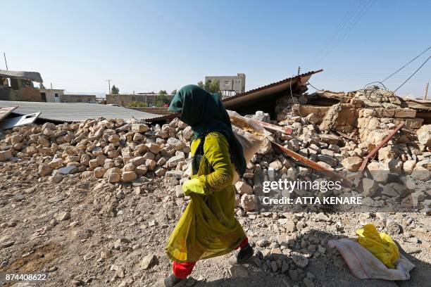 Picture taken on November 15, 2017 shows an Iranian woman walking past the rubble of a building in Kouik village near to Sarpol-e Zahab, two days...