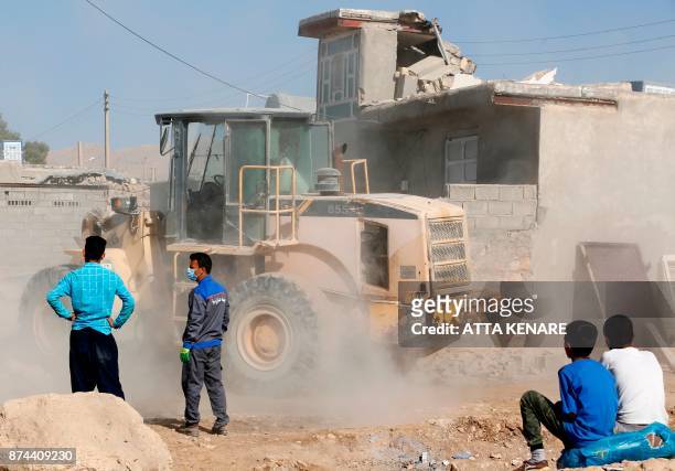 Picture taken on November 15, 2017 shows Iranian boys watching as a bulldozer clears the rubble of destroyed buildings in Kouik village near to...
