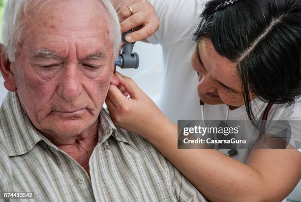 ältere mann mit einer ohr-prüfung in der arztpraxis - ear exam stock-fotos und bilder