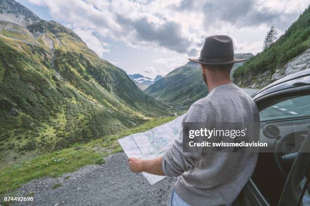 jonge man kijkt naar de routekaart in de buurt van op bergweg, zwitserland - roadmap stockfoto's en -beelden