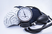 The figure of the human brain enveloped sphygmomanometer cuff with bulb (pear) and dial showing high pressure. Concept high brain or increased (raised) intracranial pressure (hypertension)
