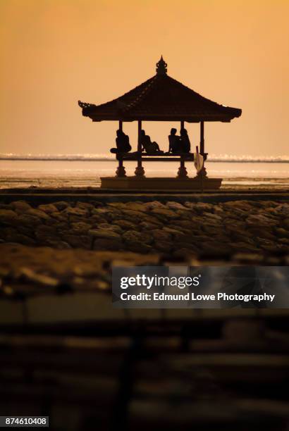 men sitting on a balinese bale gazebo during sunset. - sanur stock pictures, royalty-free photos & images