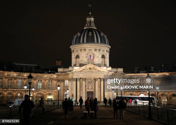 Pedestrians walk on the 'Pont des Arts' in over the River Seine in front of The 'Institute de France' in Paris at night on November 15, 2017.